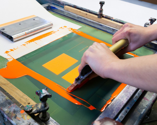 Student rakelt Farbe über Sieb