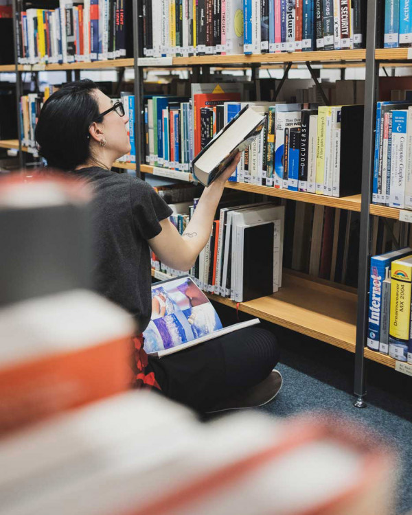 Studentin sitzend vor Bücherregal